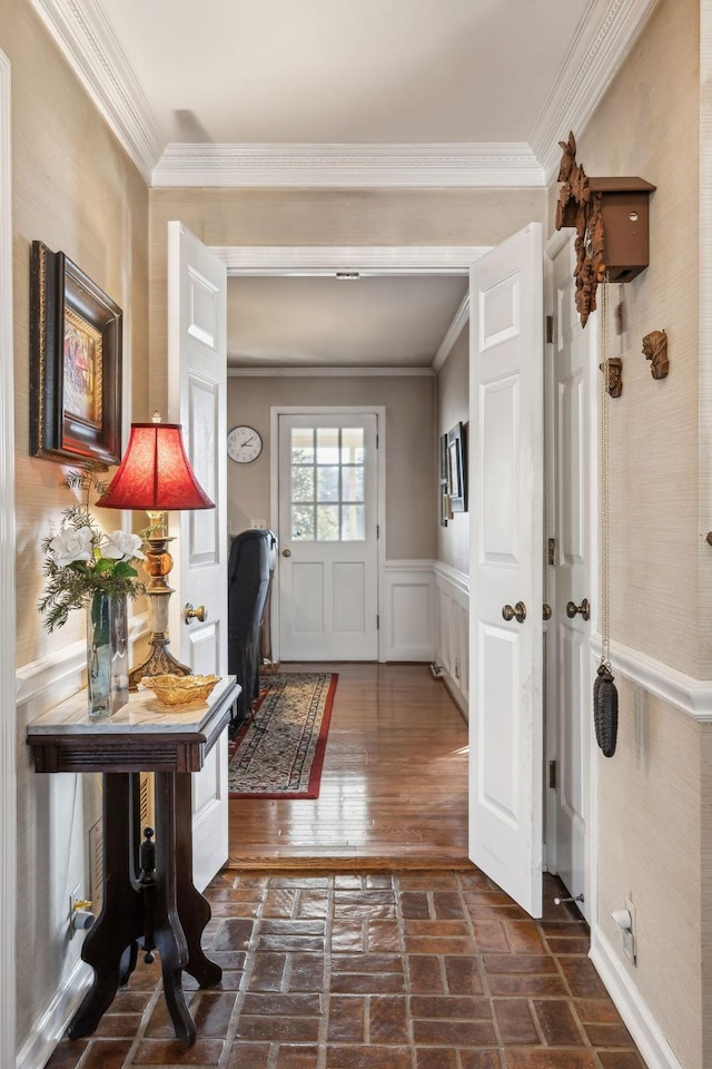 foyer with brick floor, a wainscoted wall, and crown molding