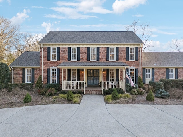 view of front of house with covered porch, a shingled roof, and brick siding