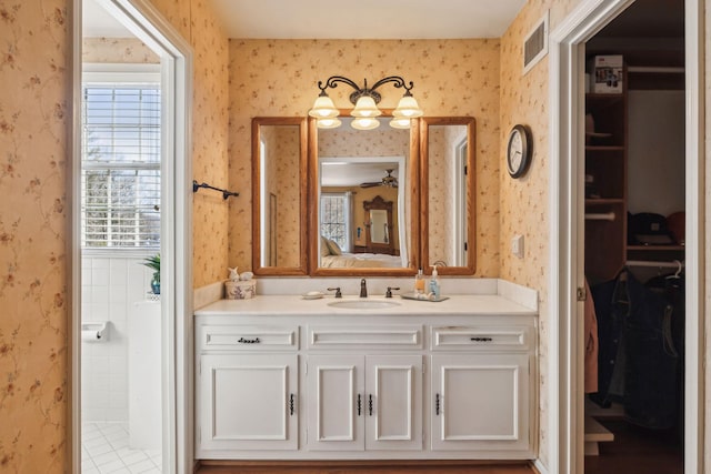 bathroom with a walk in closet, visible vents, vanity, ensuite bath, and wallpapered walls