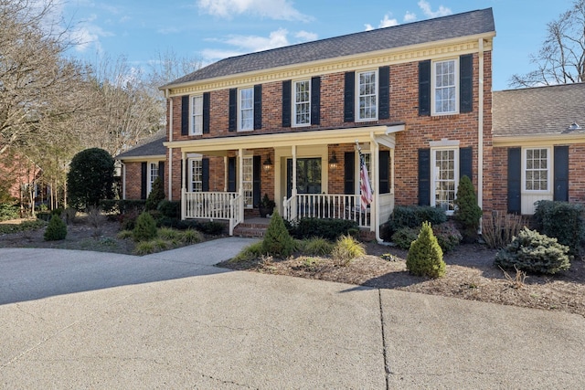 colonial inspired home with covered porch, brick siding, and roof with shingles