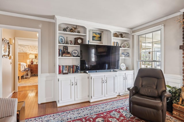 living area with light wood-type flooring, ornamental molding, and wainscoting