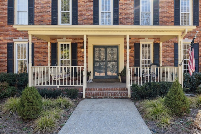 view of exterior entry featuring covered porch and brick siding