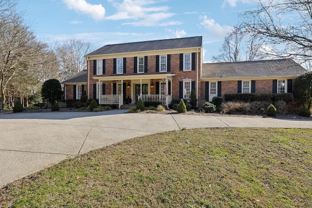 colonial home featuring a front yard, covered porch, and brick siding