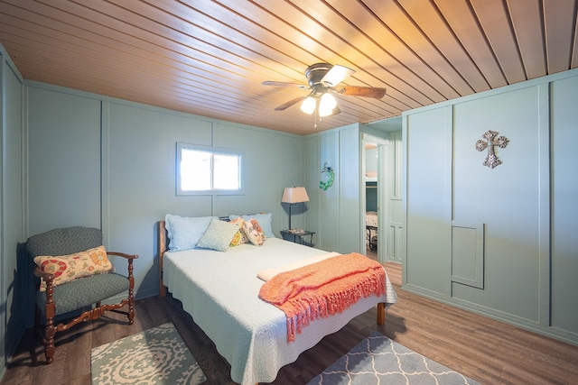 bedroom featuring ceiling fan, wood finished floors, wood ceiling, and a decorative wall