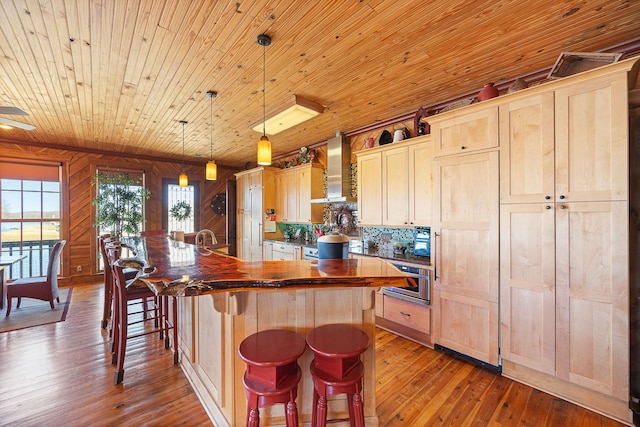 kitchen featuring light brown cabinetry, wall chimney range hood, dark countertops, and dark wood finished floors