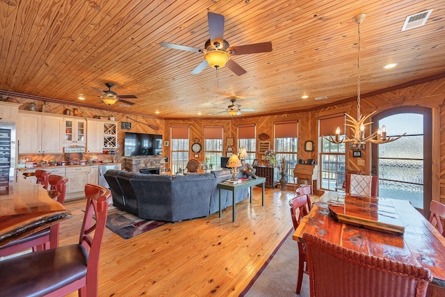 living area featuring wood ceiling, a stone fireplace, wooden walls, a chandelier, and light wood-type flooring