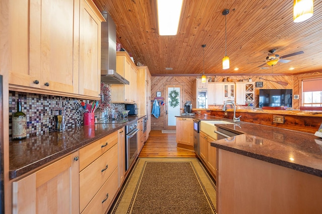 kitchen with wood ceiling, wall chimney range hood, decorative backsplash, light brown cabinetry, and dark stone countertops