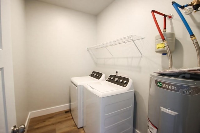 washroom with washing machine and clothes dryer, water heater, wood finished floors, laundry area, and baseboards