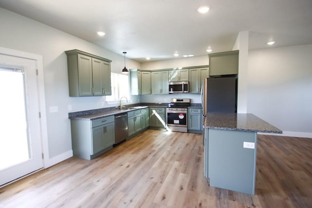 kitchen featuring recessed lighting, stainless steel appliances, a sink, dark stone counters, and light wood finished floors