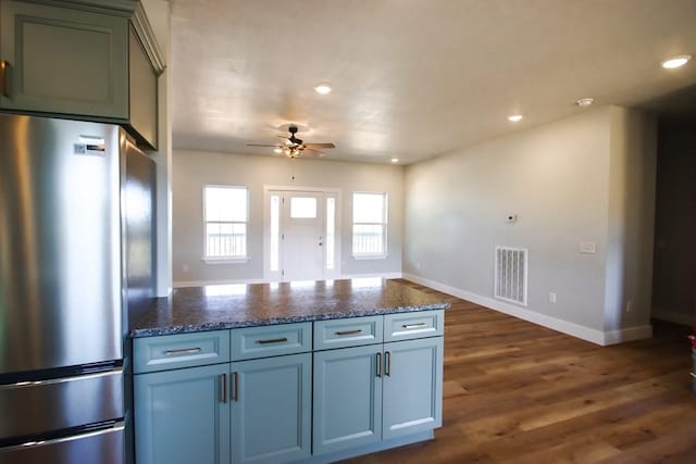 kitchen with a peninsula, visible vents, freestanding refrigerator, dark stone counters, and dark wood finished floors