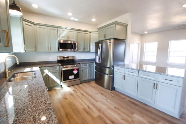 kitchen with light wood-type flooring, dark stone countertops, stainless steel appliances, and a sink