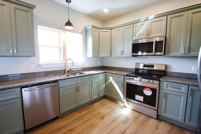 kitchen with stainless steel appliances, gray cabinets, hanging light fixtures, a sink, and light wood-type flooring