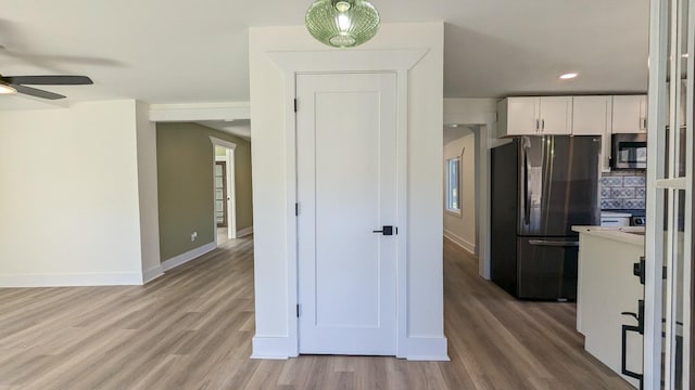 kitchen with stainless steel microwave, light wood-style flooring, freestanding refrigerator, white cabinets, and baseboards