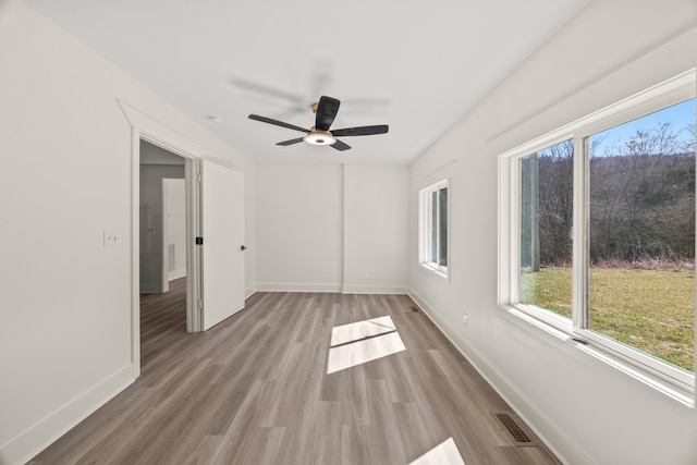 spare room featuring light wood-style floors, visible vents, baseboards, and a ceiling fan