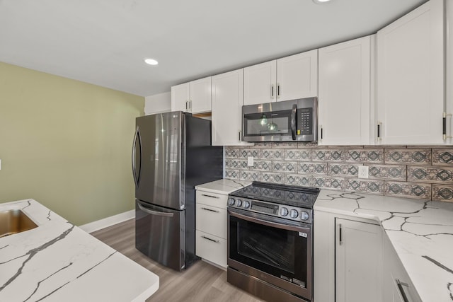 kitchen featuring light stone counters, stainless steel appliances, backsplash, white cabinetry, and light wood-type flooring