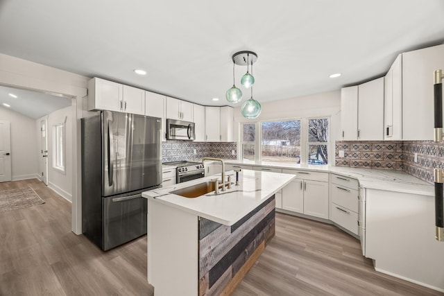 kitchen with stainless steel appliances, a sink, white cabinets, decorative backsplash, and light wood finished floors