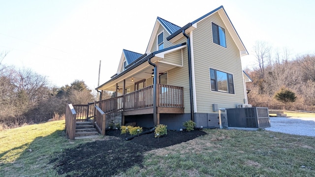 exterior space featuring metal roof, a lawn, a wooden deck, and central air condition unit