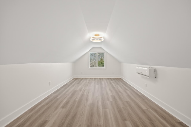 additional living space with light wood-type flooring, baseboards, vaulted ceiling, and a wall mounted air conditioner