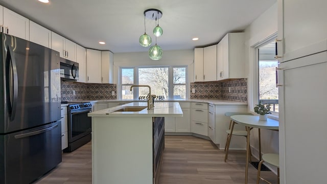 kitchen with a center island with sink, stainless steel microwave, black range with electric stovetop, freestanding refrigerator, and a sink