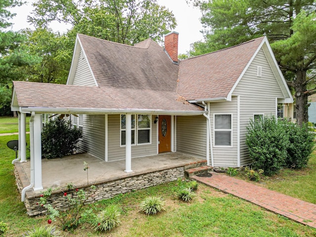 view of front of home with a shingled roof, a chimney, and a front yard