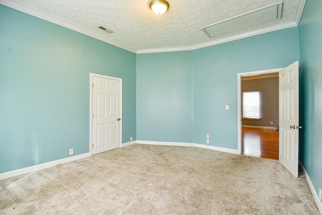 carpeted empty room featuring a textured ceiling, visible vents, baseboards, attic access, and crown molding