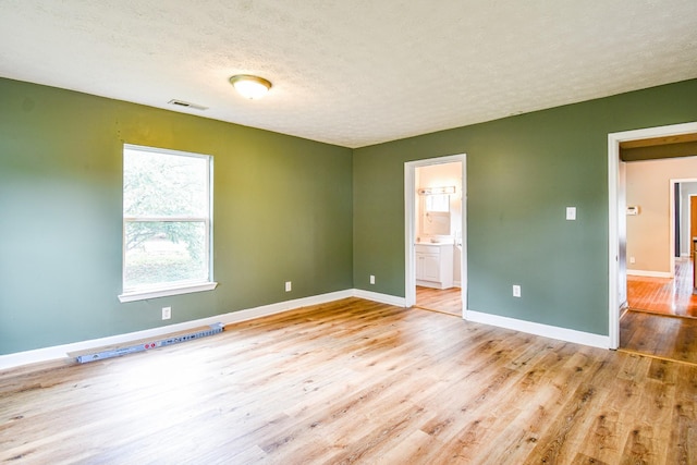 unfurnished room with visible vents, a textured ceiling, baseboards, and wood finished floors