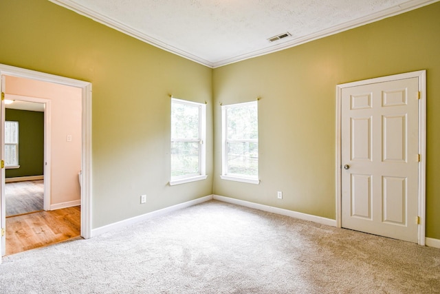 empty room with ornamental molding, carpet, visible vents, and baseboards