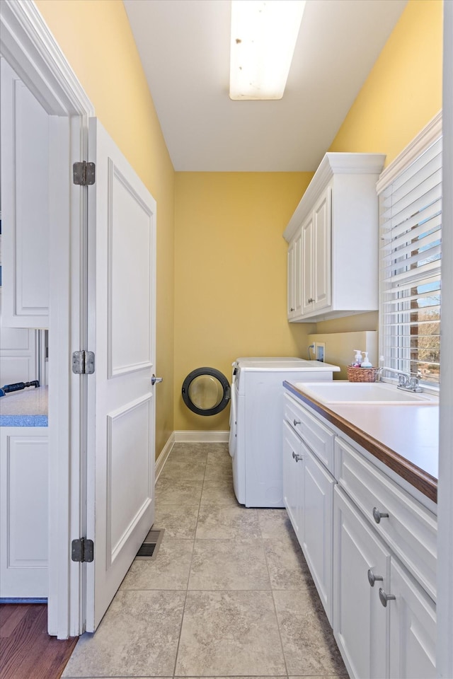 clothes washing area with cabinet space, visible vents, a sink, washer / dryer, and baseboards