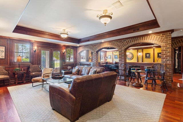 living room with crown molding, a tray ceiling, arched walkways, and wood finished floors