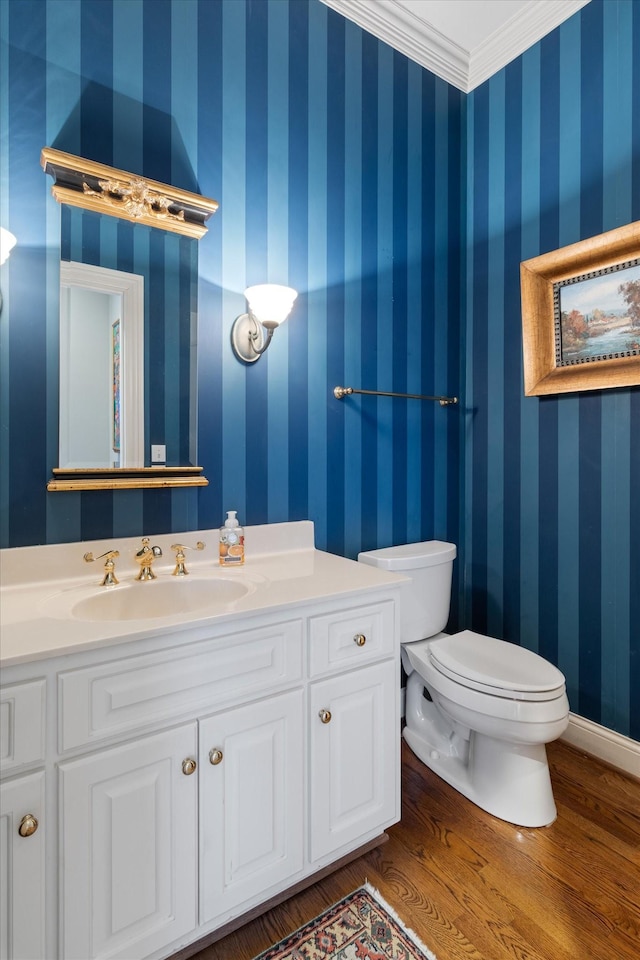 half bathroom featuring toilet, vanity, wood finished floors, baseboards, and wallpapered walls