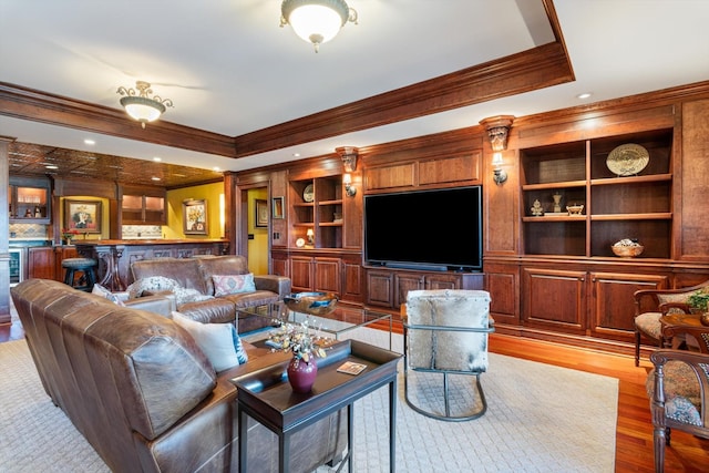 living room with a raised ceiling, ornamental molding, wood finished floors, and wet bar