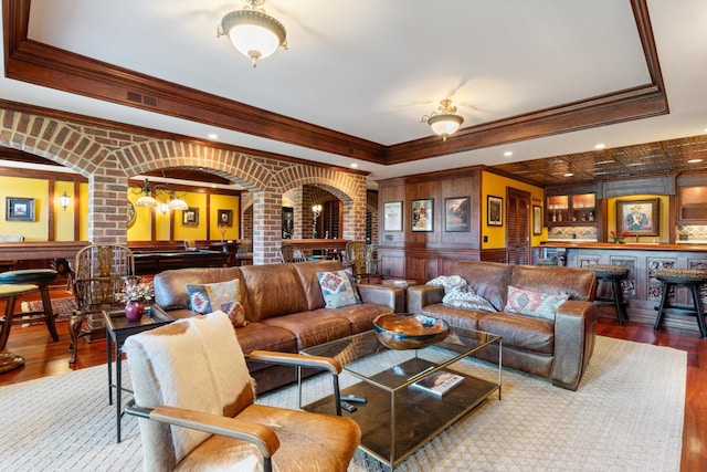 living area featuring arched walkways, a raised ceiling, pool table, a bar, and wood finished floors