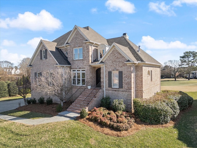 view of front of home featuring brick siding, stairs, roof with shingles, a front lawn, and a chimney