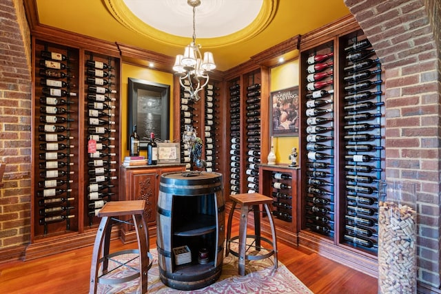 wine cellar with brick wall, a chandelier, a raised ceiling, and wood finished floors