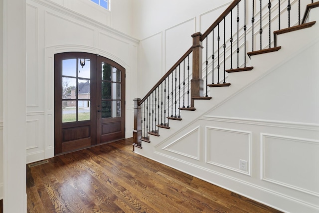 entrance foyer featuring dark wood-style floors, french doors, a healthy amount of sunlight, and a decorative wall