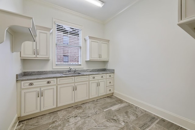 kitchen featuring baseboards, cream cabinets, light countertops, crown molding, and a sink