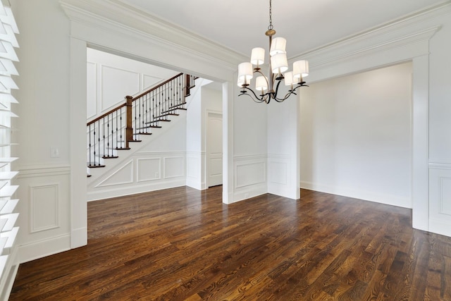 unfurnished dining area featuring dark wood-style floors, crown molding, a decorative wall, stairway, and a chandelier