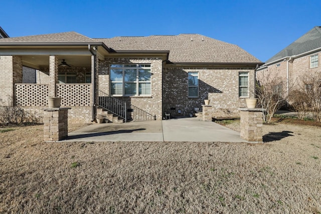 rear view of property with a shingled roof, brick siding, a patio, and a ceiling fan