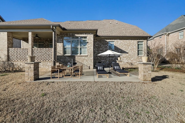 back of property with roof with shingles, a ceiling fan, a patio, and brick siding