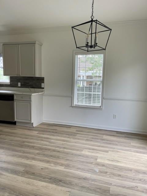 unfurnished dining area with a chandelier, baseboards, light wood-style flooring, and crown molding