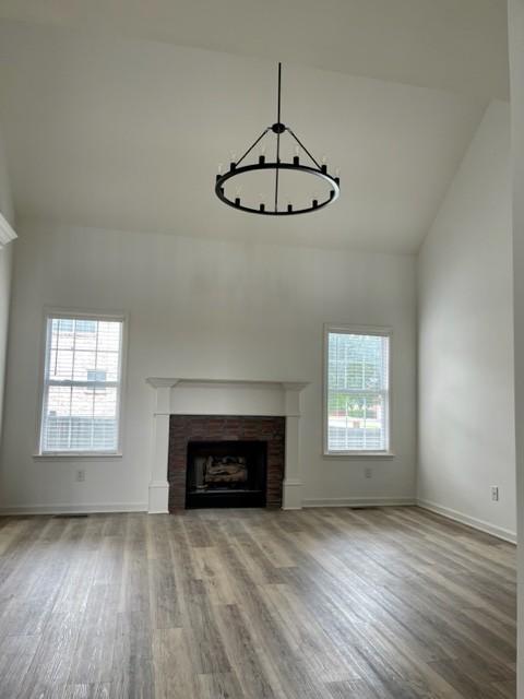 unfurnished living room with high vaulted ceiling, a fireplace, baseboards, and wood finished floors