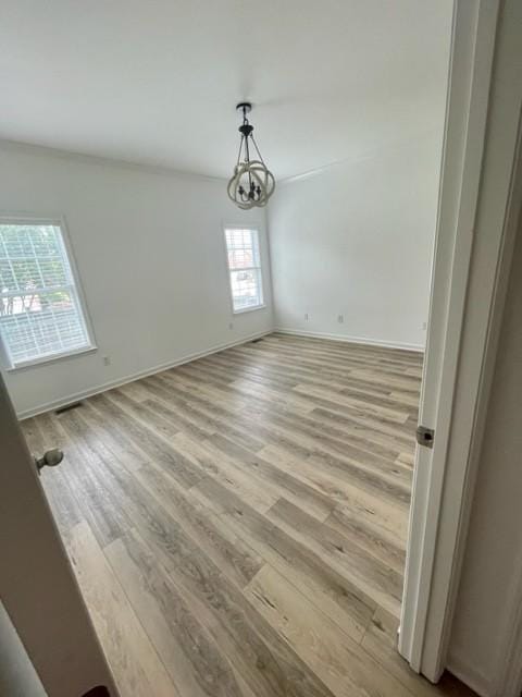 spare room with baseboards, an inviting chandelier, and light wood-style floors