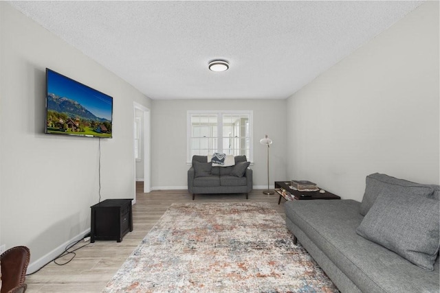 living area featuring a textured ceiling, light wood-style flooring, and baseboards