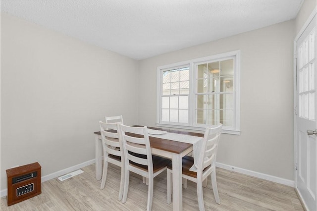 dining area featuring a textured ceiling, light wood-style flooring, visible vents, and baseboards