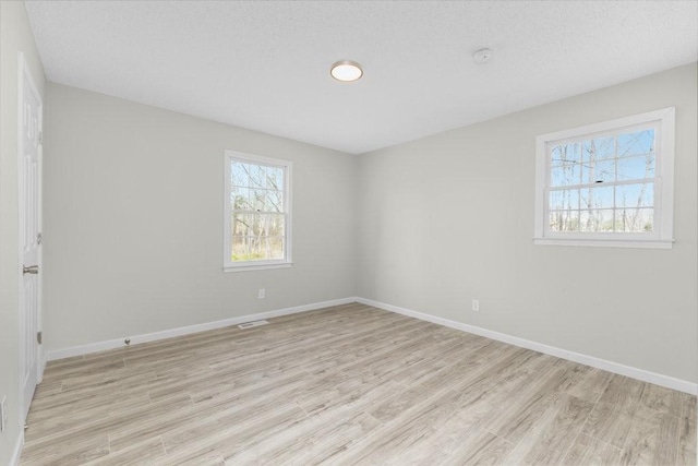 empty room with a textured ceiling, light wood finished floors, visible vents, and baseboards