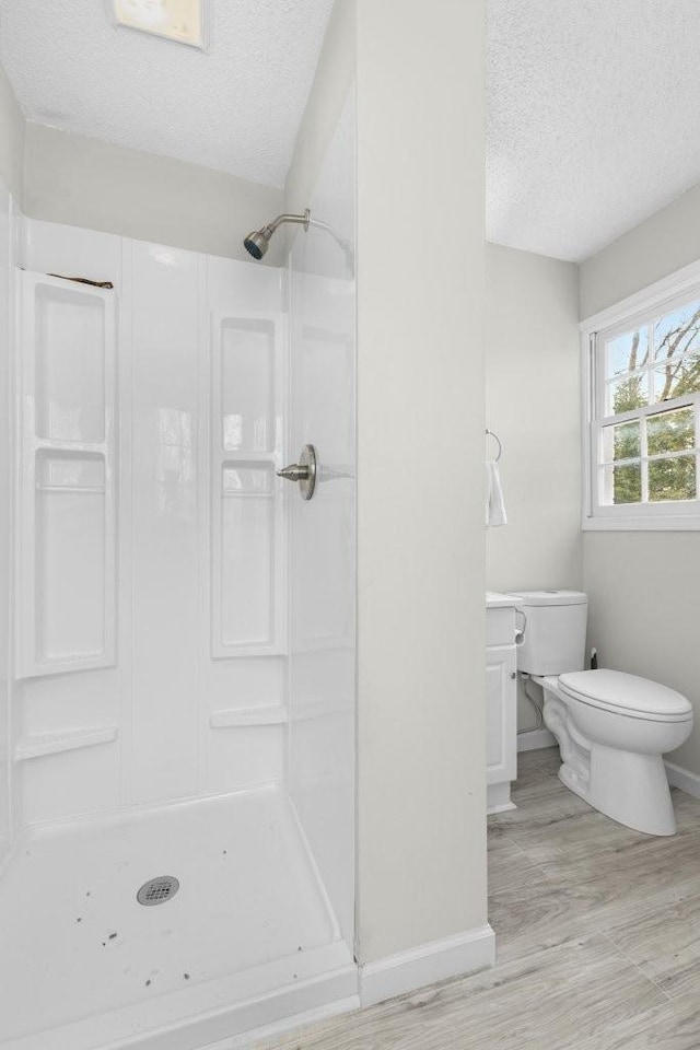 full bath with toilet, a stall shower, a textured ceiling, wood finished floors, and baseboards