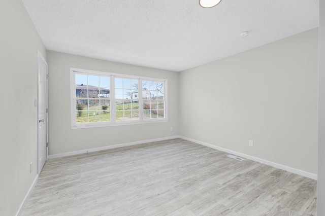 unfurnished room with baseboards, light wood-style flooring, visible vents, and a textured ceiling