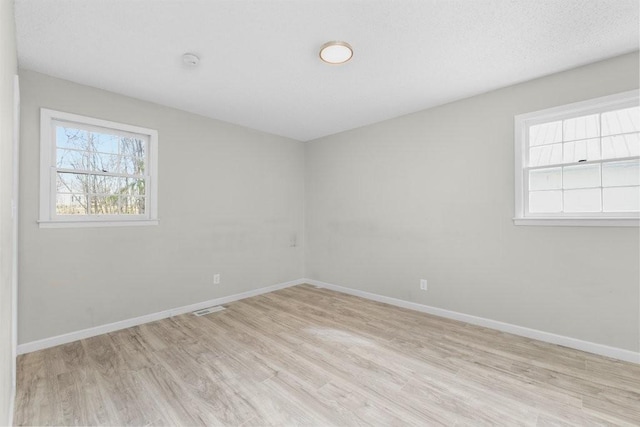 empty room with visible vents, light wood-style flooring, baseboards, and a textured ceiling