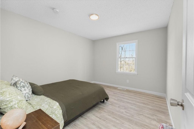 bedroom with a textured ceiling, light wood-type flooring, and baseboards