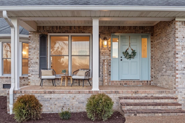 property entrance featuring a porch, a shingled roof, and brick siding